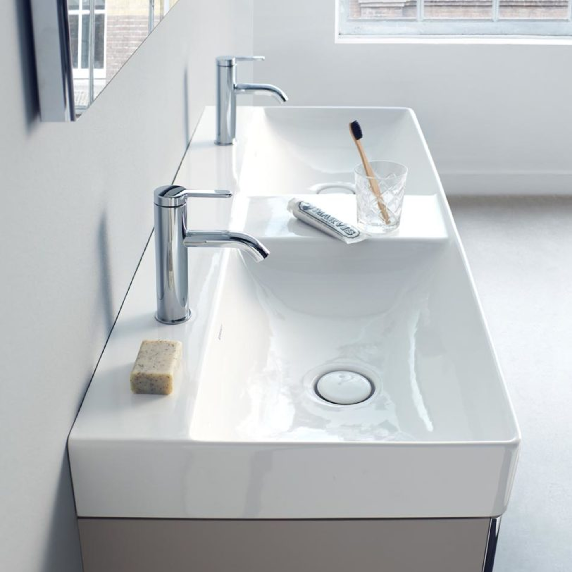 Lavabo Duravit colgado en una pared azul, con un espejo iluminado encima; armario oscuro a la izquierda, toalla y obra de art