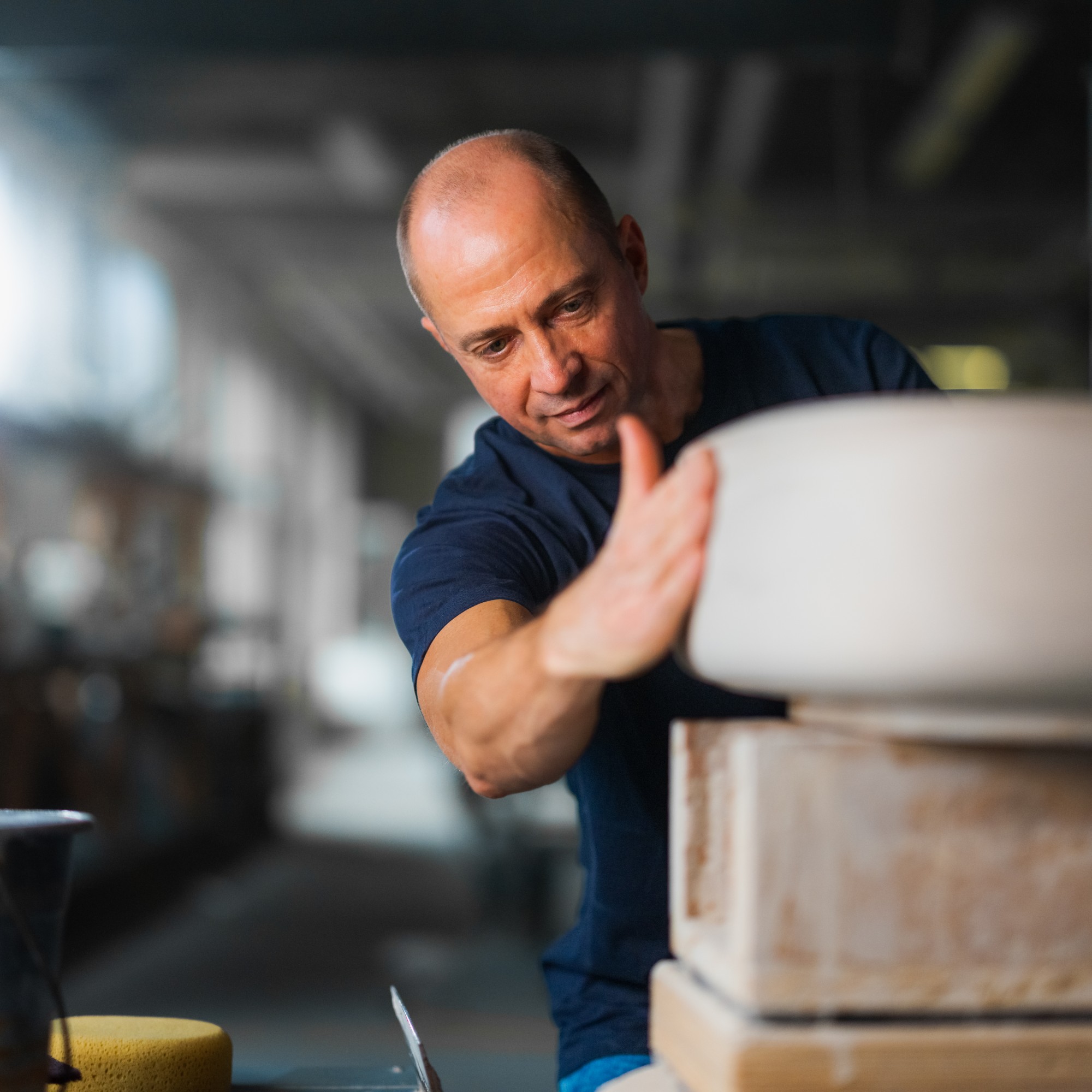A man is working on a ceramic mold in a Duravit workshop, with a dimly lit, out-of-focus background