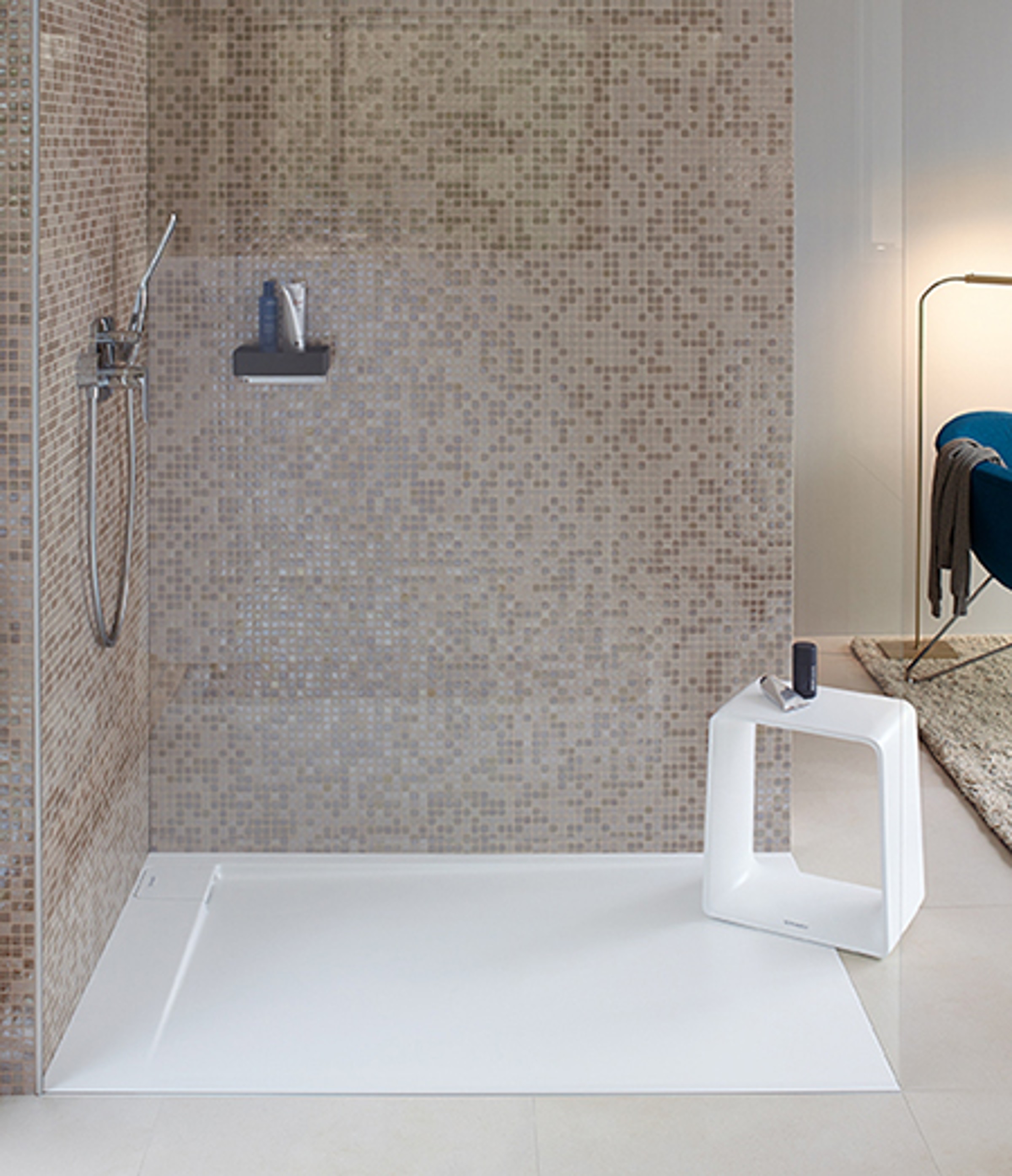 A walk-in shower with a glass wall. The adjacent walls are tiled with mosaic.