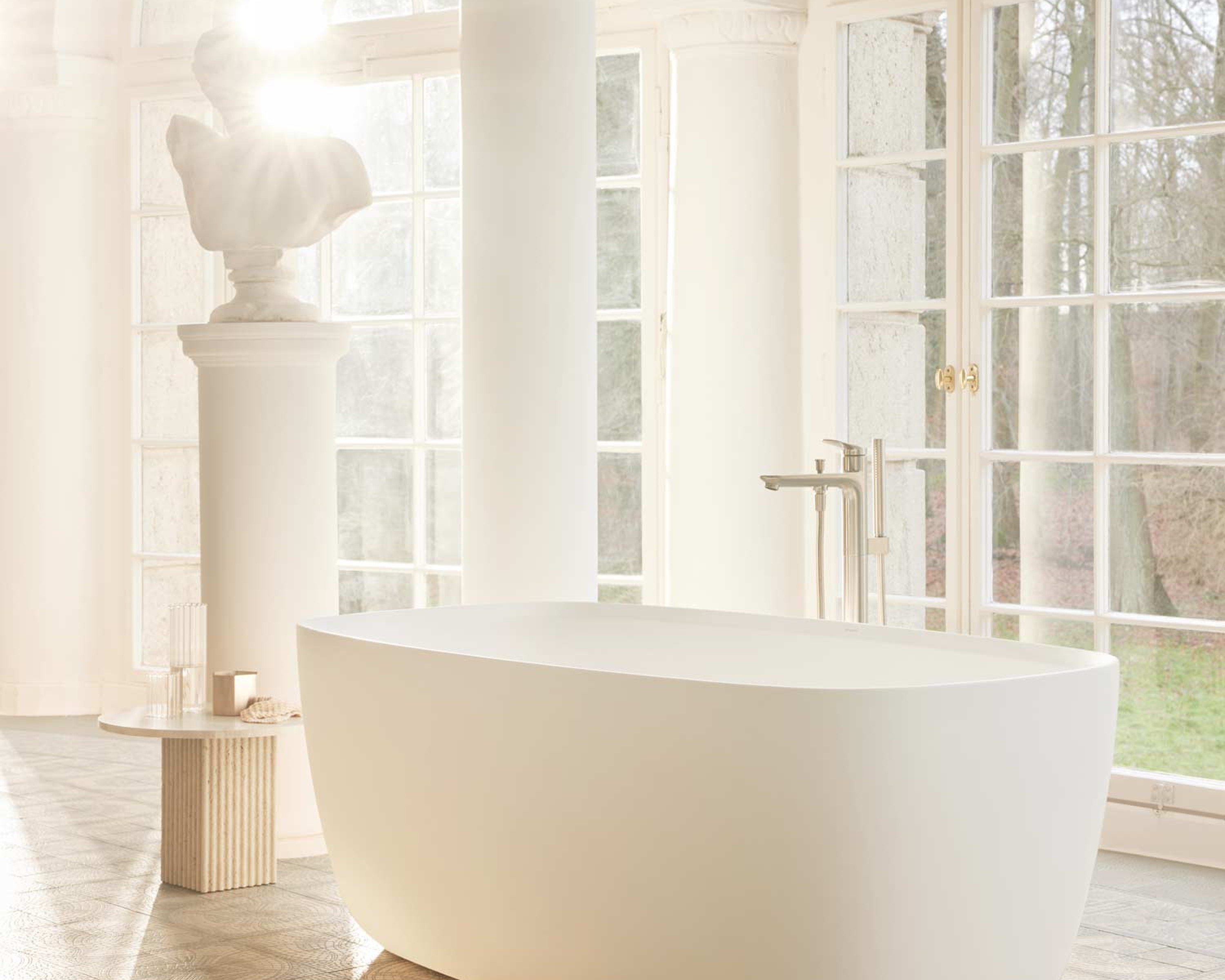 Freistehende Badewanne der Serie Duravit Aurena, daneben eine Skulptur