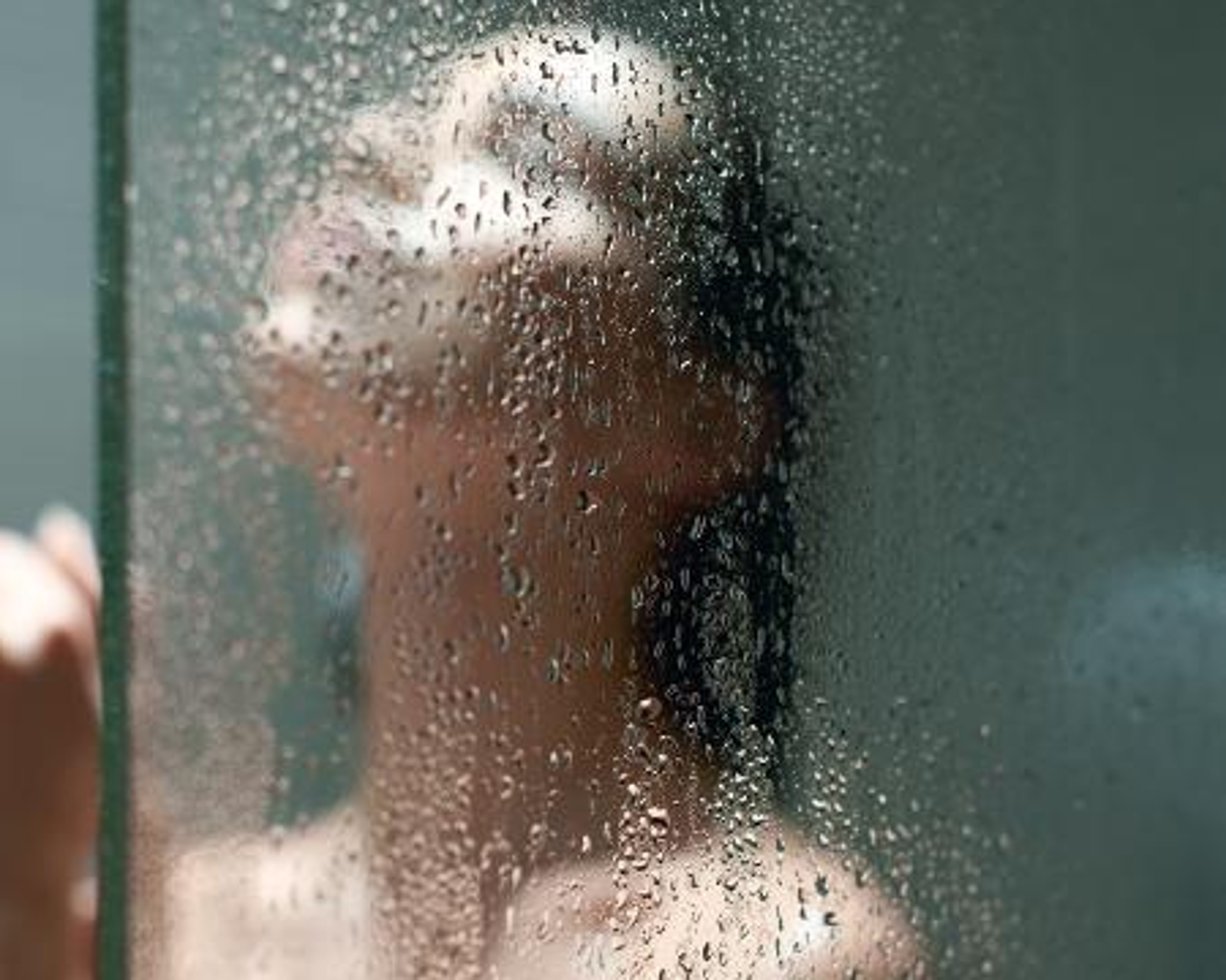 Woman behind wet glass pane of a shower