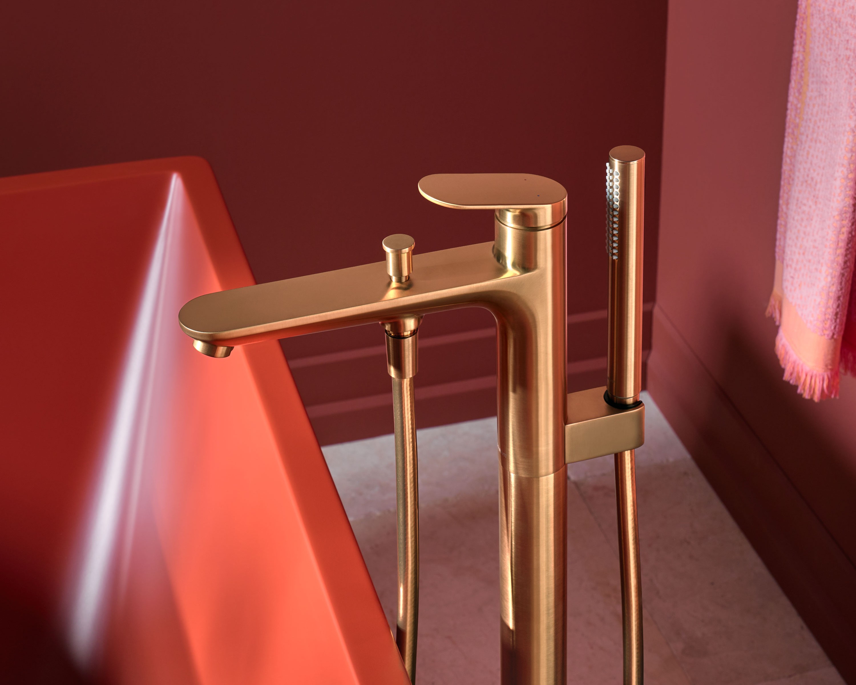 Freestanding bathtub faucet from the Duravit Wave series in brushed bronze next to a DuraSquare bathtub in cinnamon red