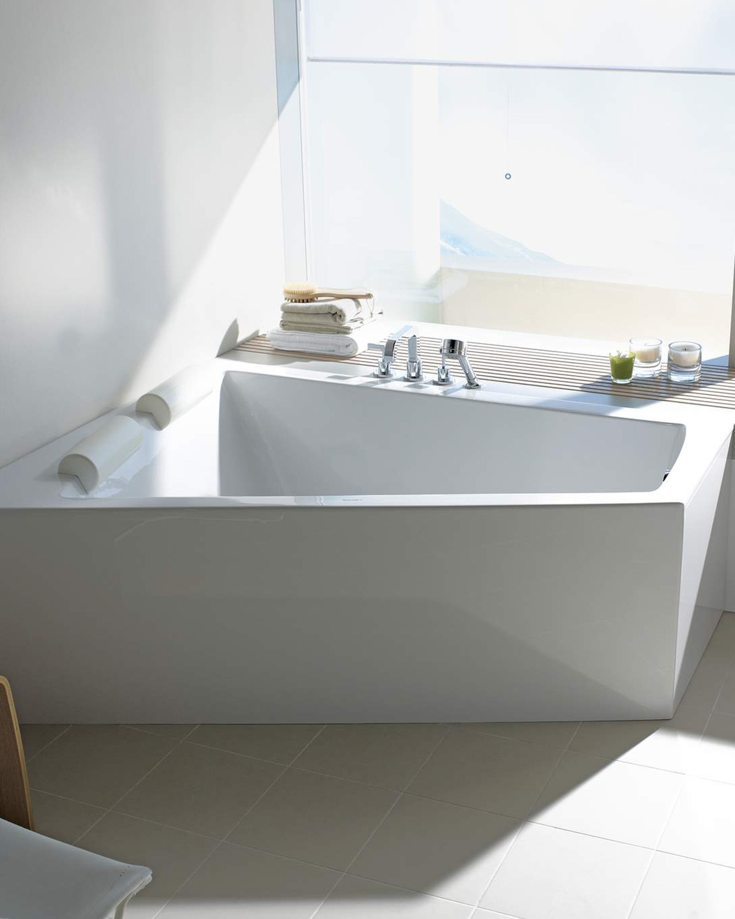 A white corner bathtub in a trapezoidal shape. Behind it, a large window.