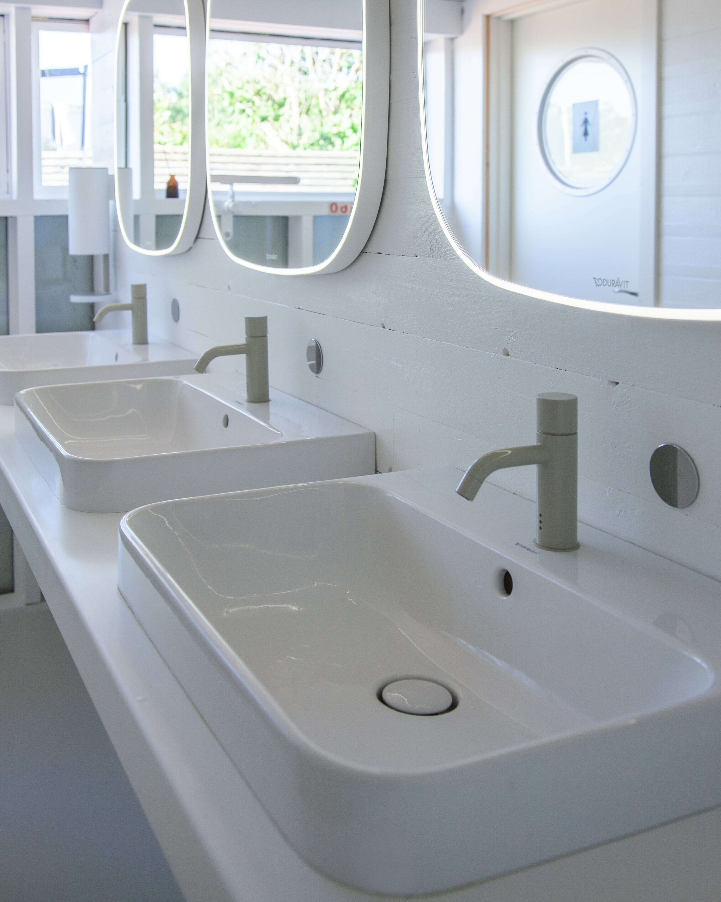 Weiße Aufsatzwaschbecken und abgerundete Spiegel von Duravit im Waschraum des Badehauses