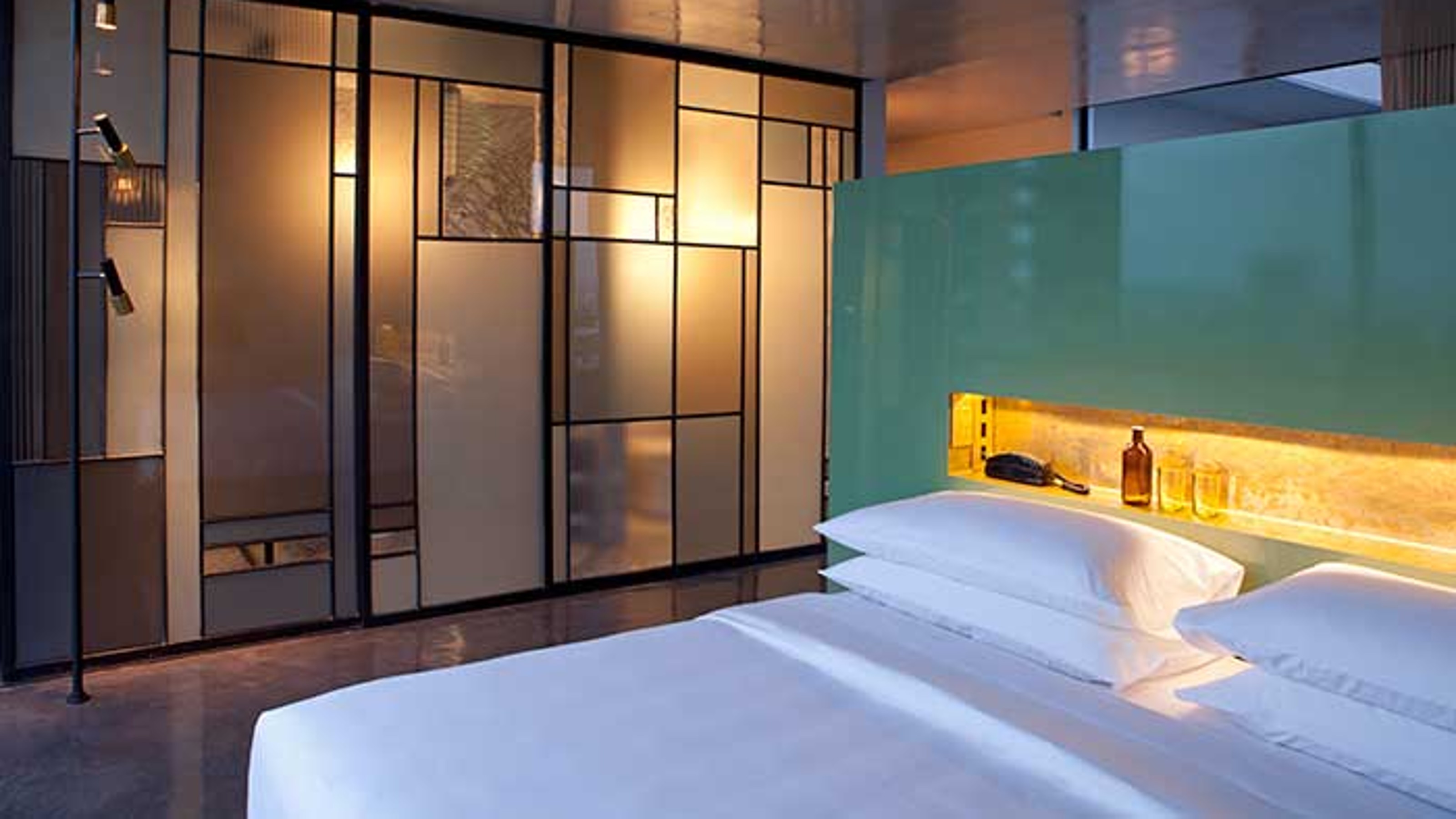 Casa Fayette, hotel room, bed on the right in the foreground, bathroom with colourful glass wall in the background