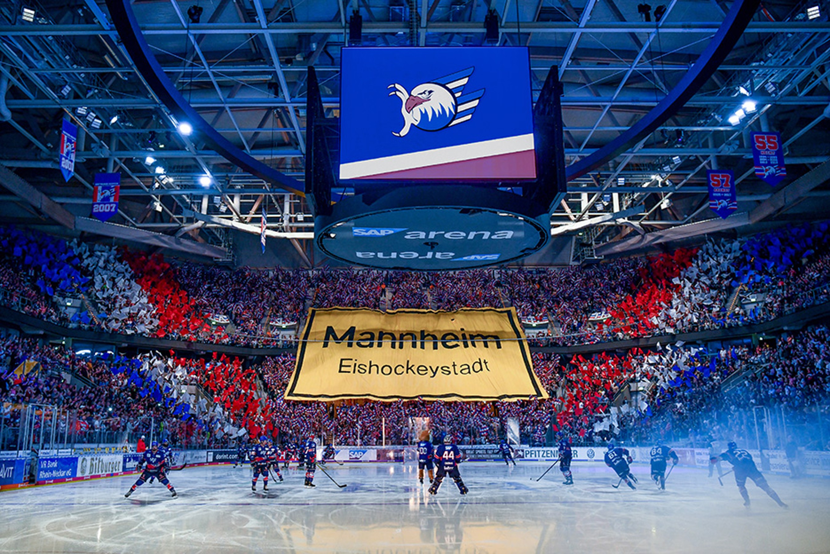 SAP Arena Mannheim during an ice hockey game with many visitors waving flags and holding up a banner with the words ‘Mannheim Eishockeystadt’ (Mannheim ice hockey city)