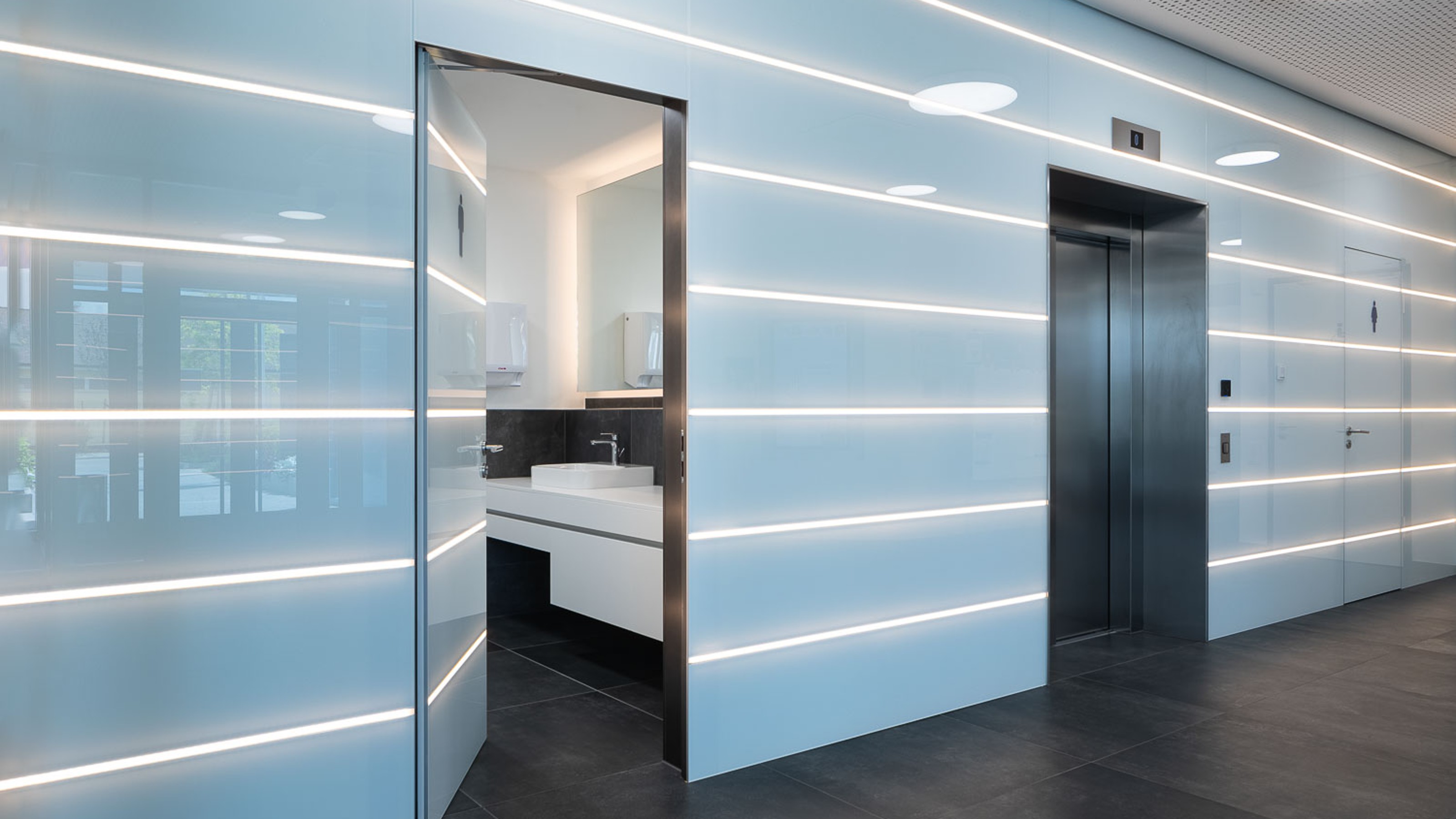 SLR Academy, illuminated walls in the hallway with view through the door into the public toilet