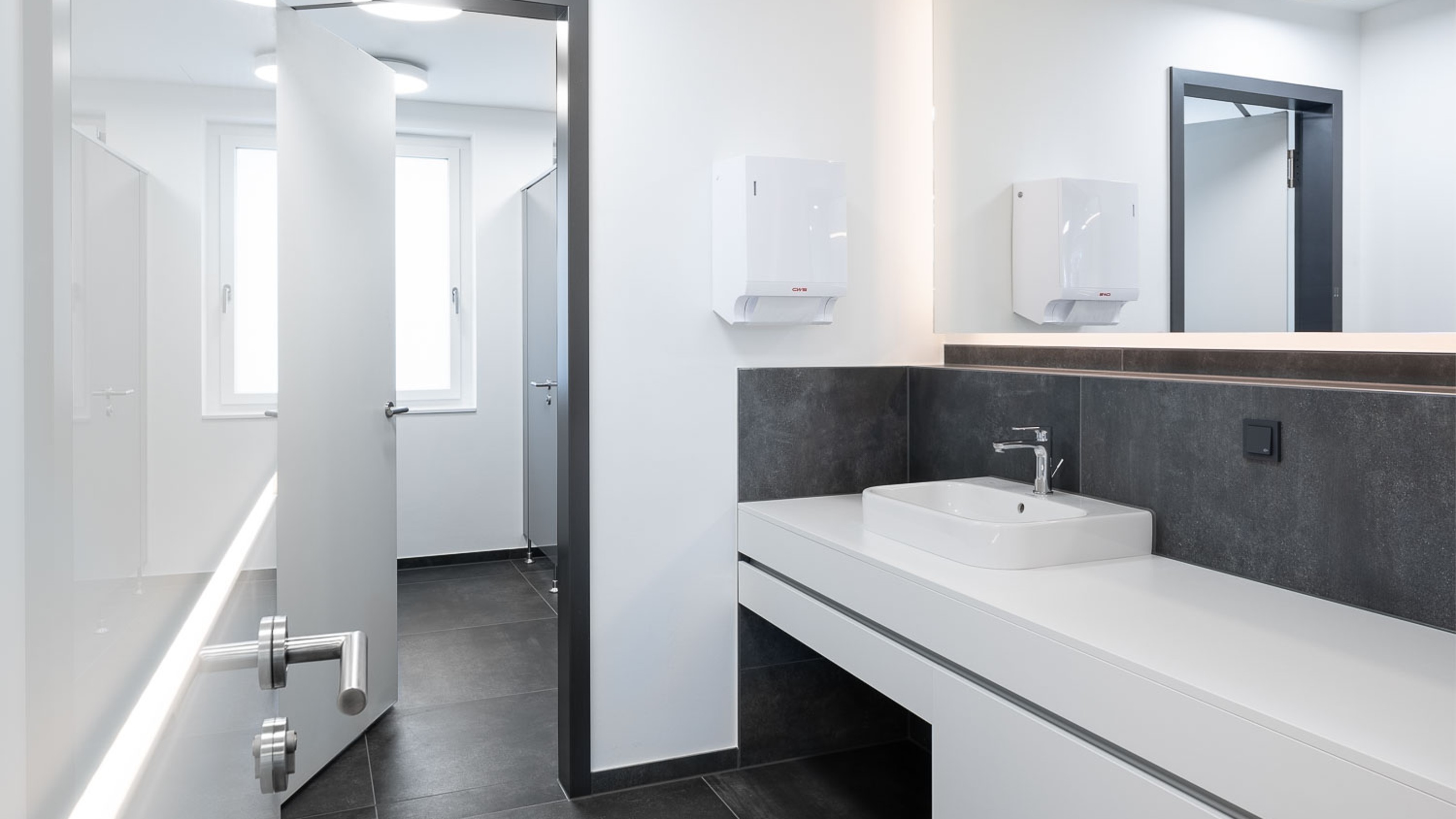 SLR Academy, public toilet with washbasin on the right and toilet cubicles in the background
