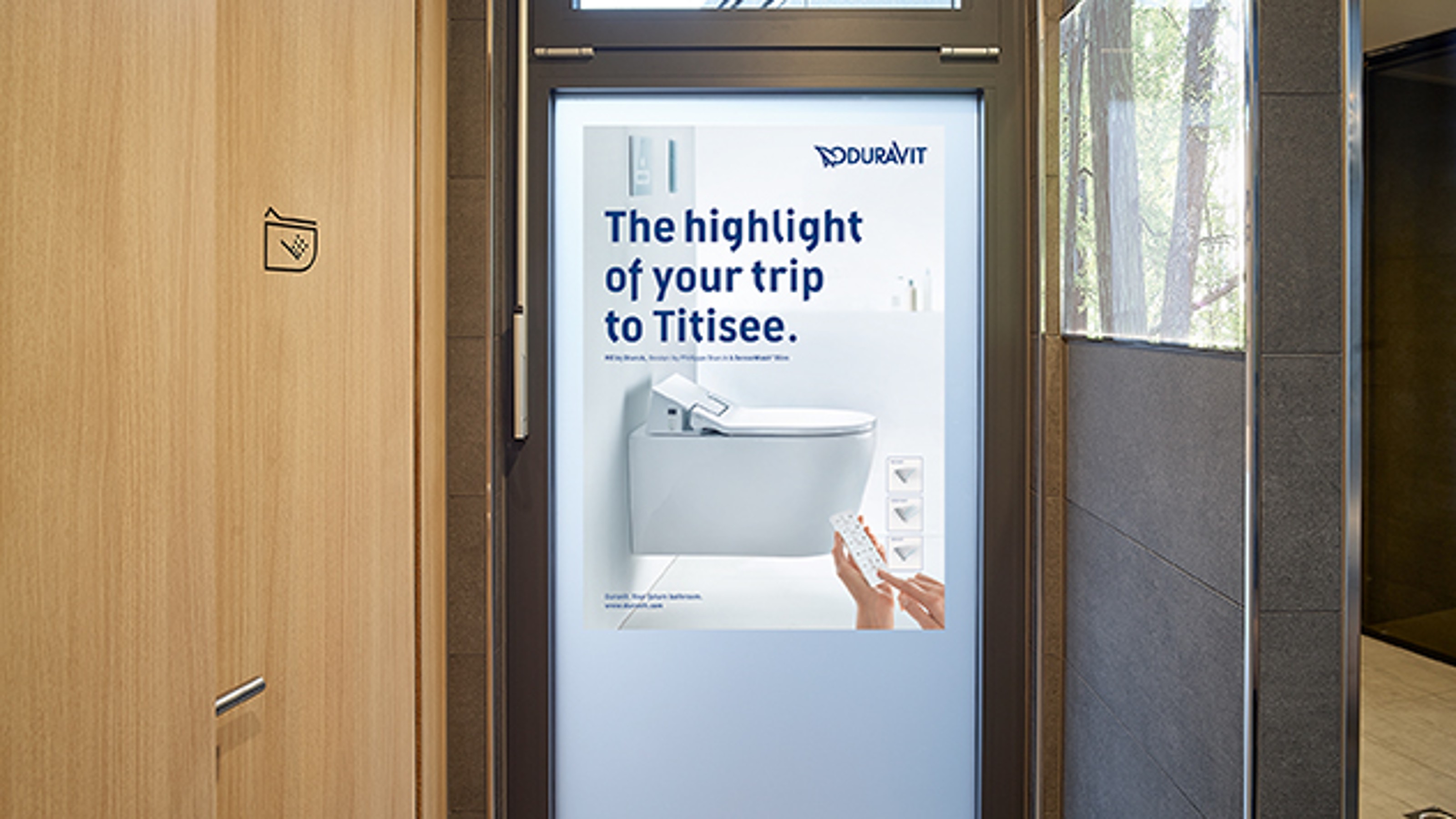Toilet facilities in Titisee from the inside, view of an entrance door with a poster on the subject of SensoWash® by Duravit, toilet cubicle on the left with SensoWash® icon on the door