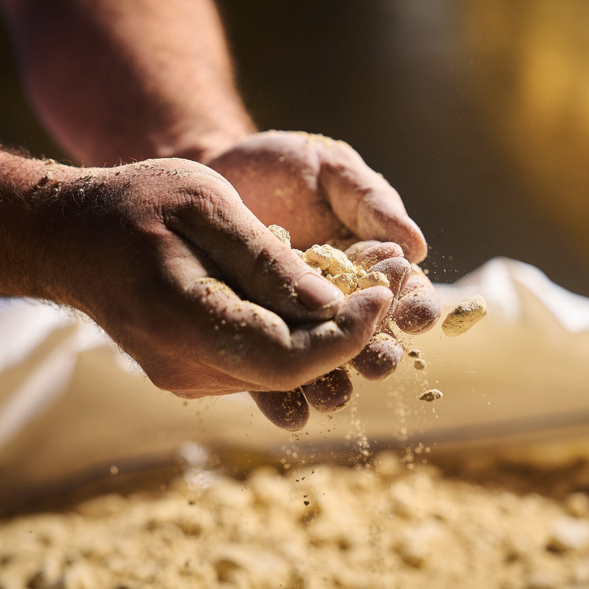 Hands scatter powder into a sack; Duravit employee checks material quality in an industrial environment.
