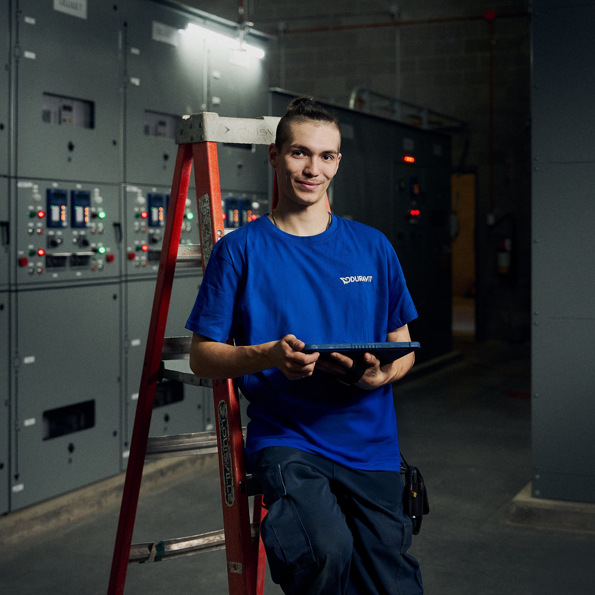 A man is leaning against a stepladder in a machine room at the Duravit factory, holding a tablet in his hand.