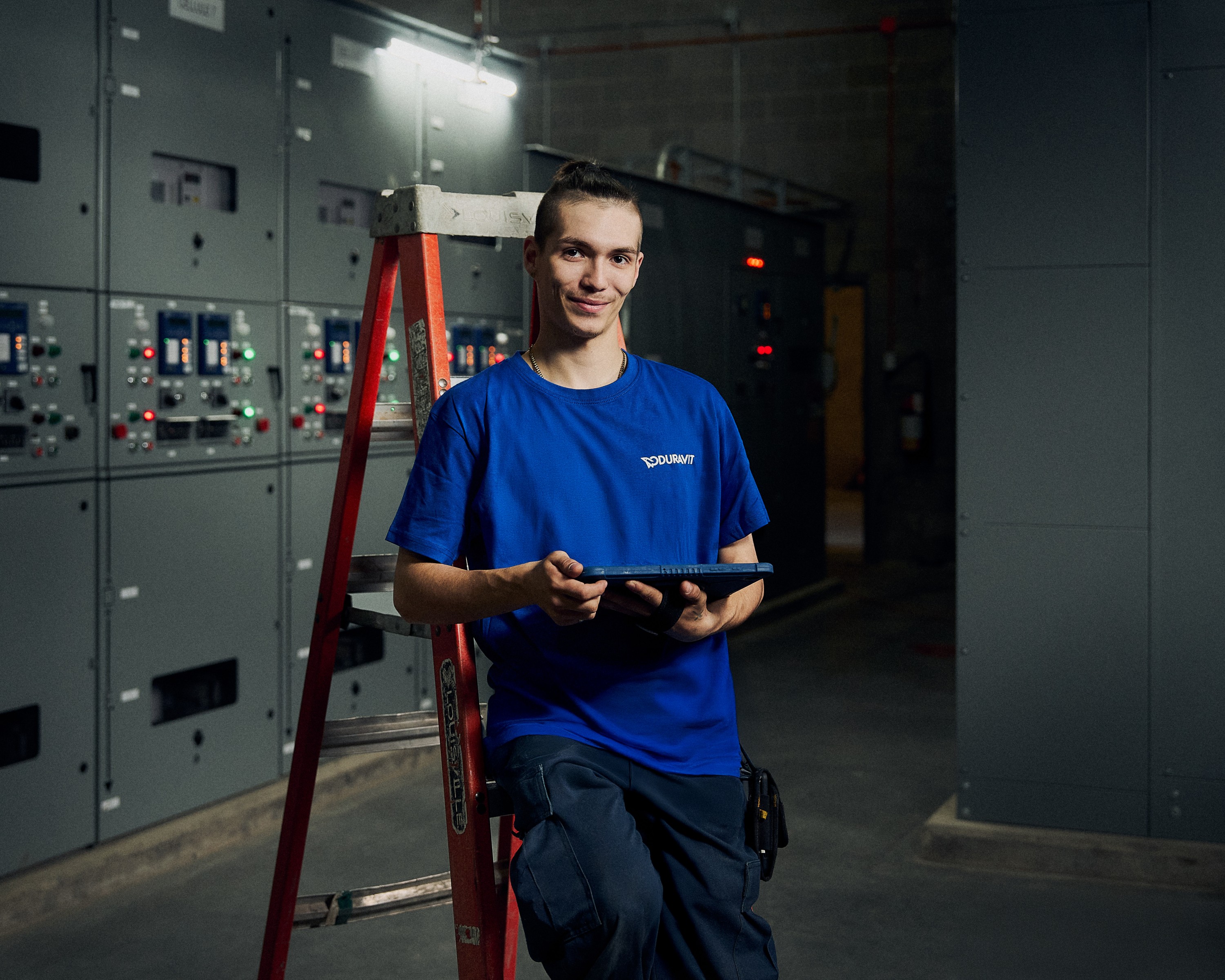 Mitarbeiter lehnt in einem Maschinenraum an eine Leiter mit einem Tablet in der Hand