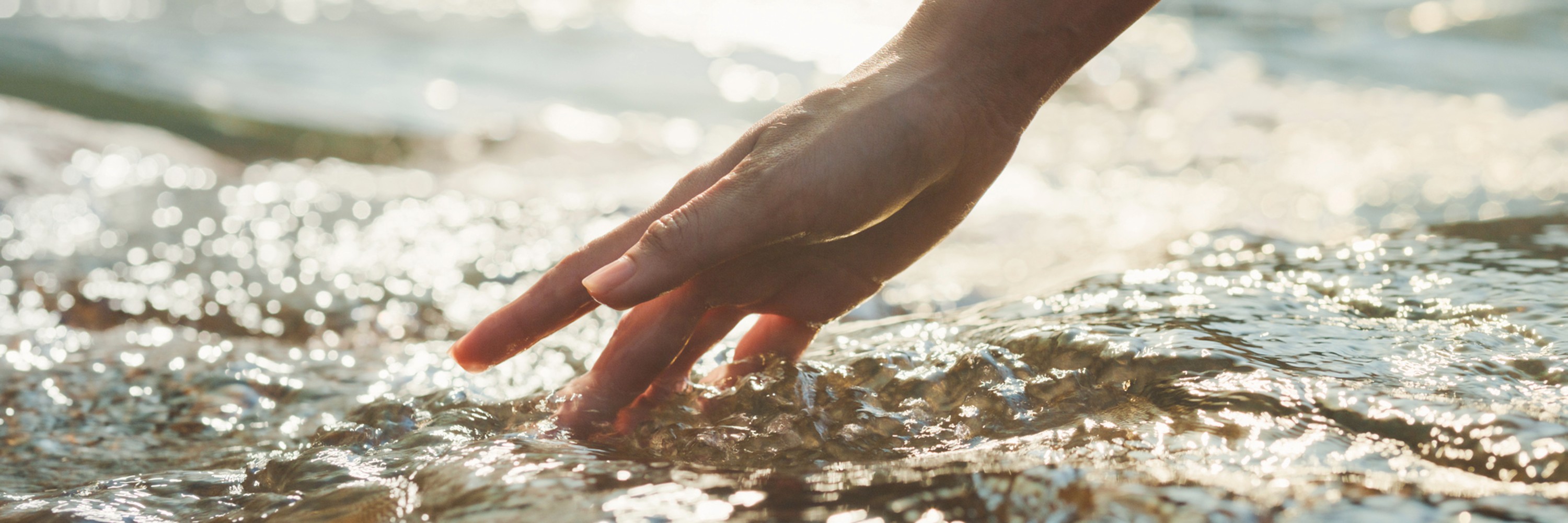 A woman's hand touches the flowing water in a river